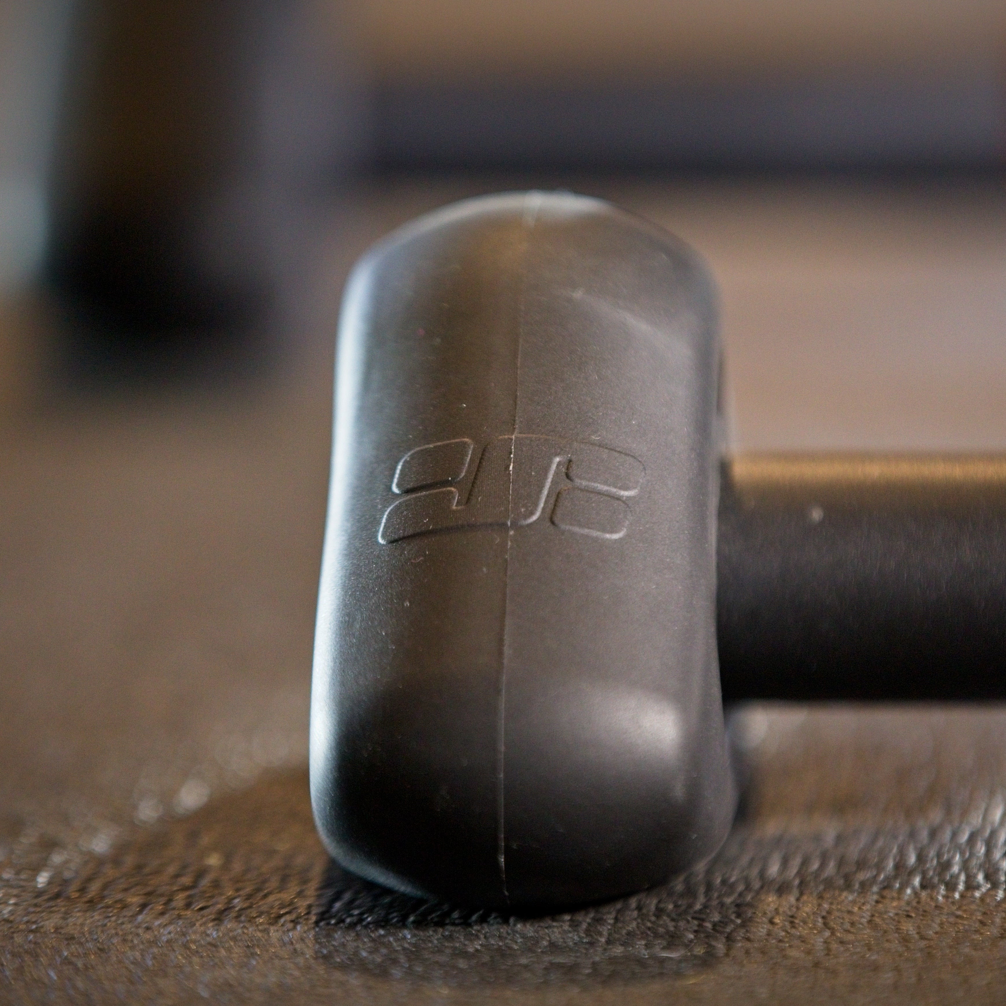 Close-up of a black foam hammer with a white stylized logo on the handle, resting on a textured dark surface.